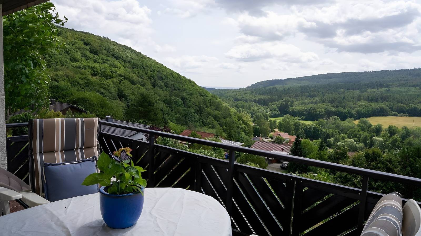 Balkon mit Tisch und Hochlehner, Blick über bewaldete Hänge ins Tal