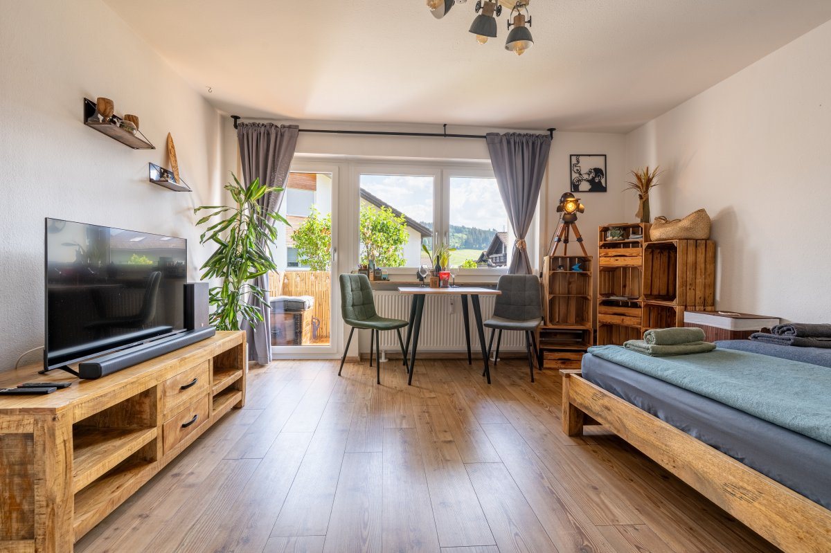 Wohnraum mit Holzbett, Esstisch am Fenster und Fernseher