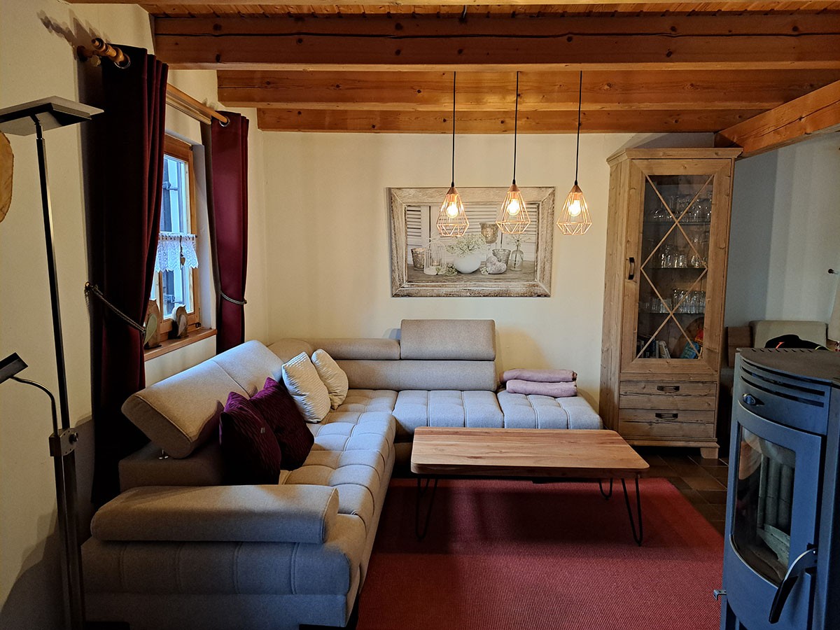 Wohnzimmer mit Ecksofa, Holzbalkendecke und Kaminofen