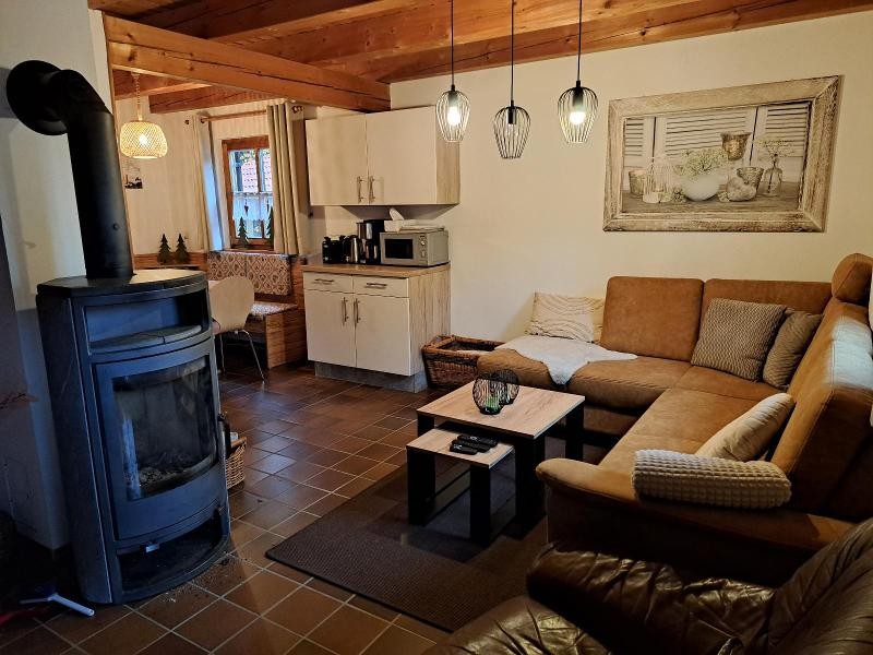 Wohnzimmer mit Holzofen und Ecksofa, dahinter die Wohnküche