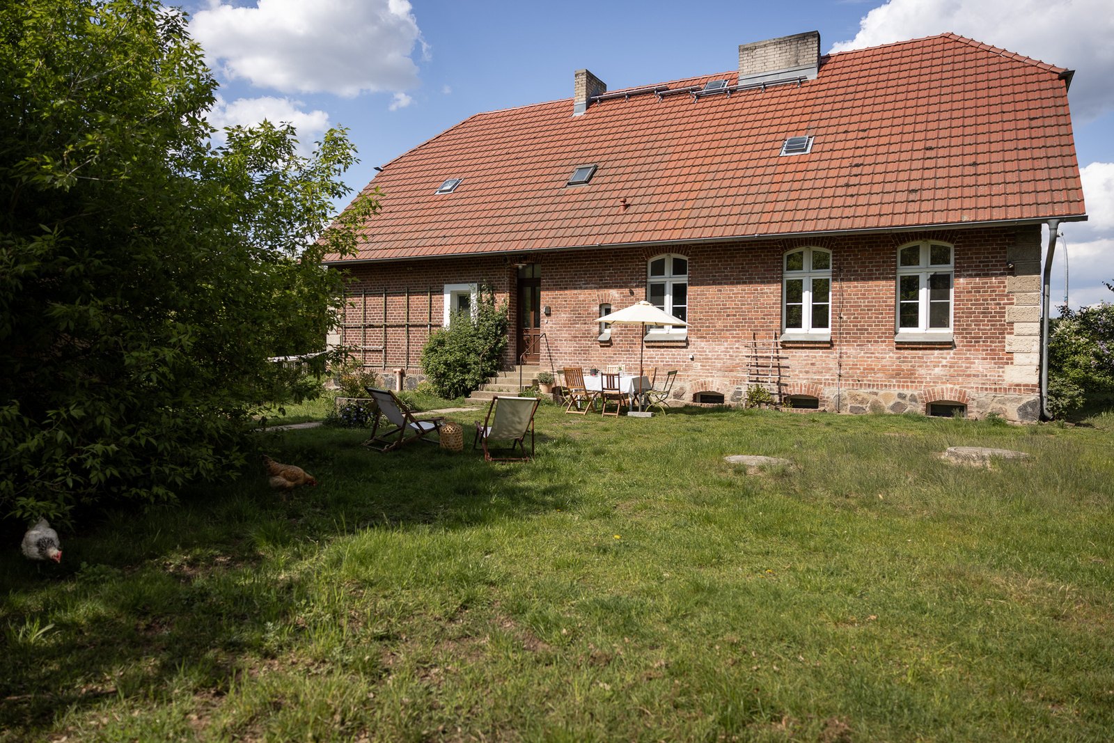 Die Alte Schule bei Kyritz von der Gartenseite, davor Liegestühle und Hühner auf der Wiese