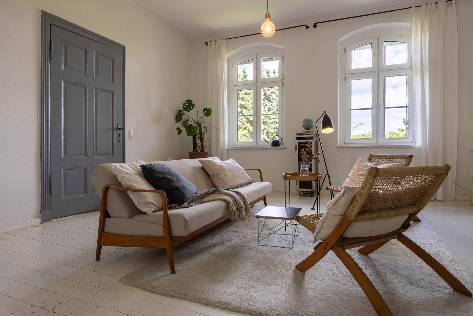 Wohnzimmer mit Sofa, zwei geflochtenen Sesseln und hohen Rundbogenfenstern