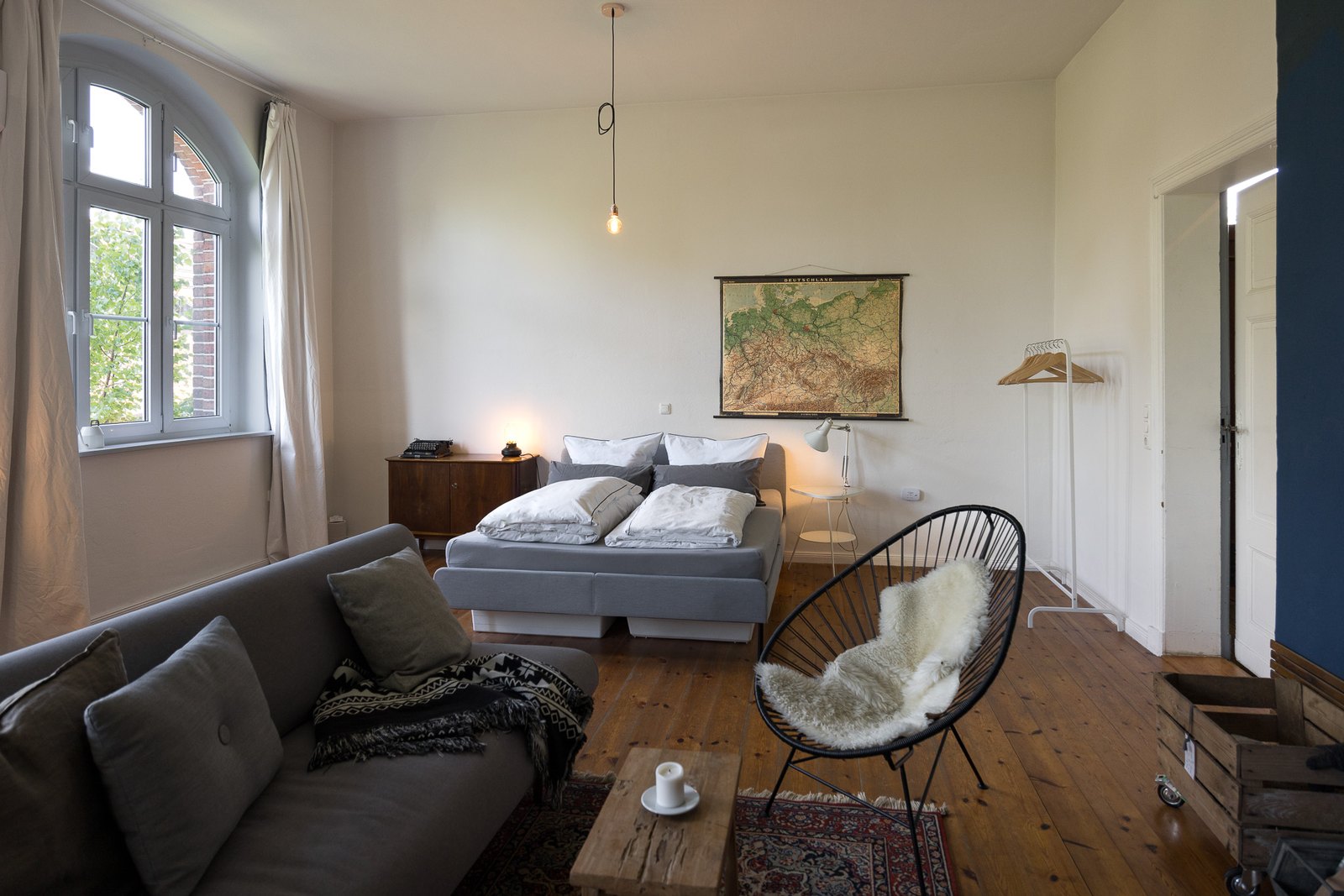 Doppelbett mit alter Deutschlandkarte an der Wand, vorn Sofa und Sessel