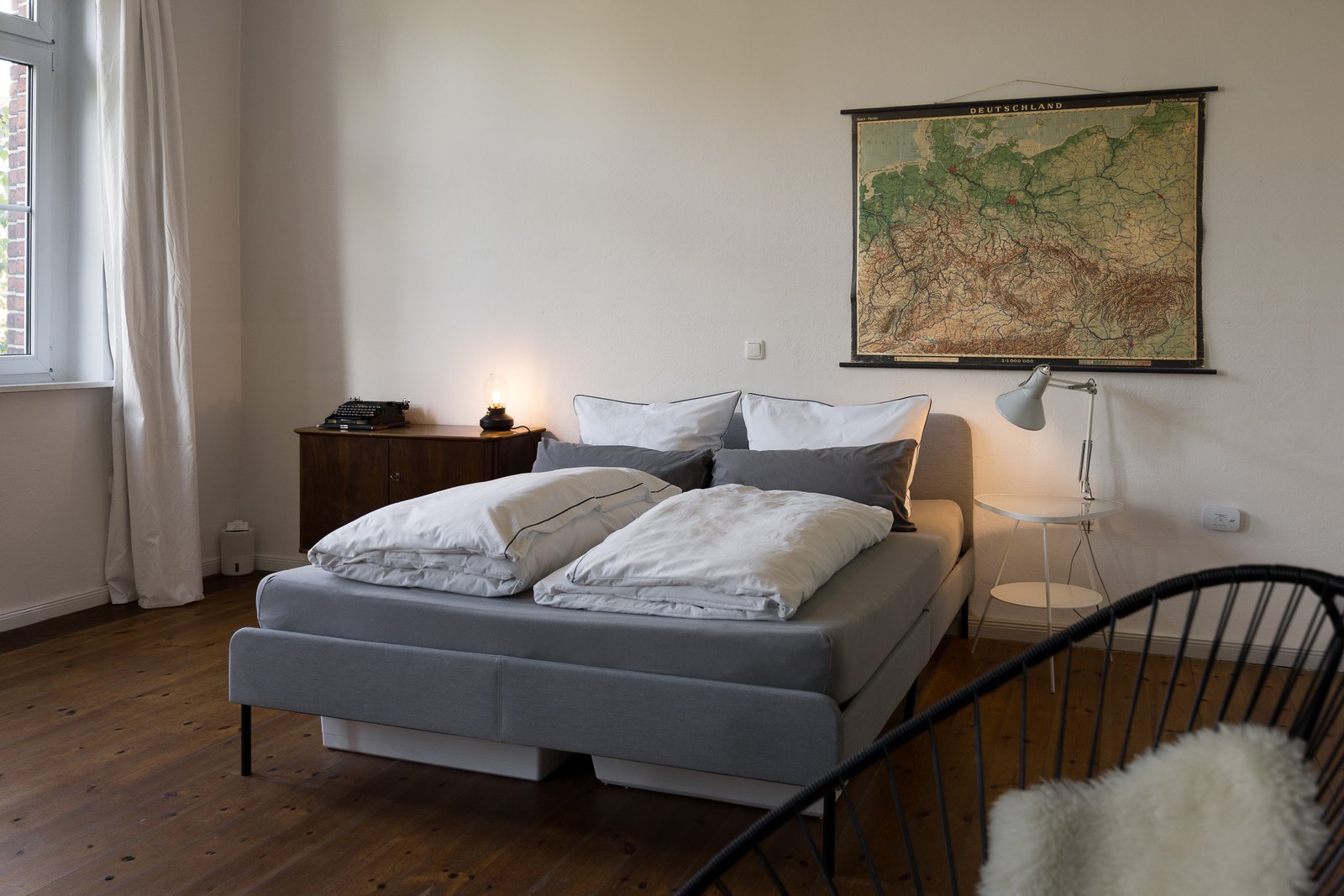Doppelbett mit Leselampe, daneben eine Kommode mit alter Schreibmaschine