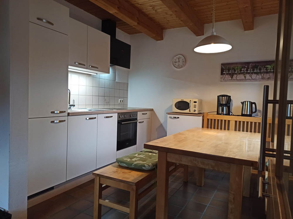 Wohnküche mit Backofen, Mikrowelle, Kaffeemaschine und Esstisch mit Bank