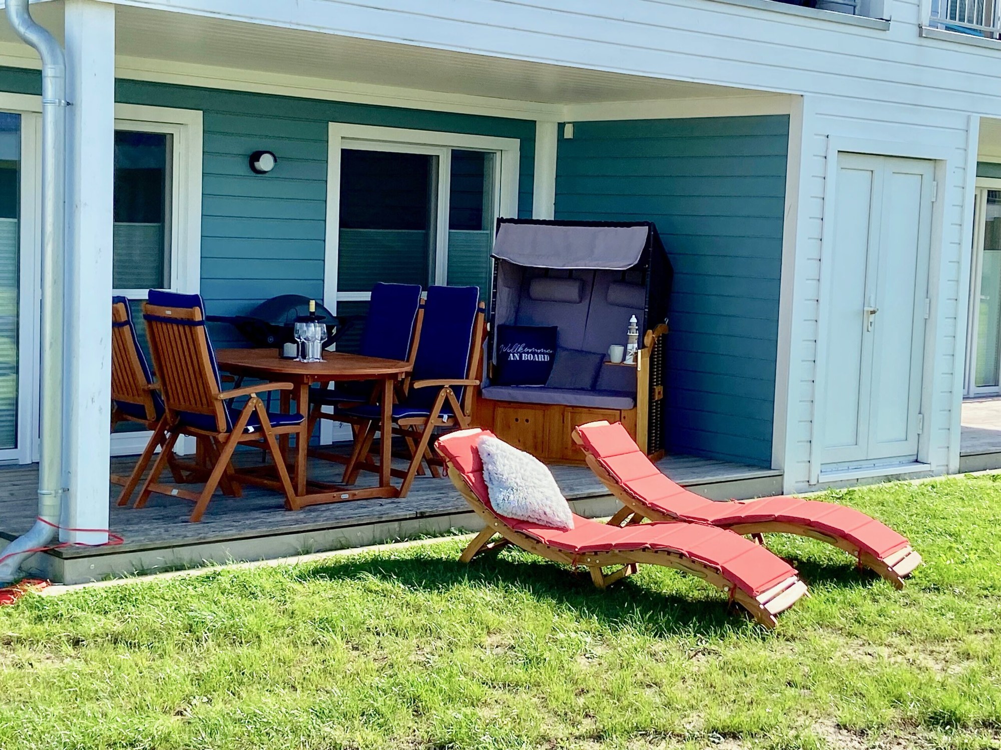 Überdachte Terrasse mit Strandkorb, Gartenmöbeln und Liegen auf dem Rasen